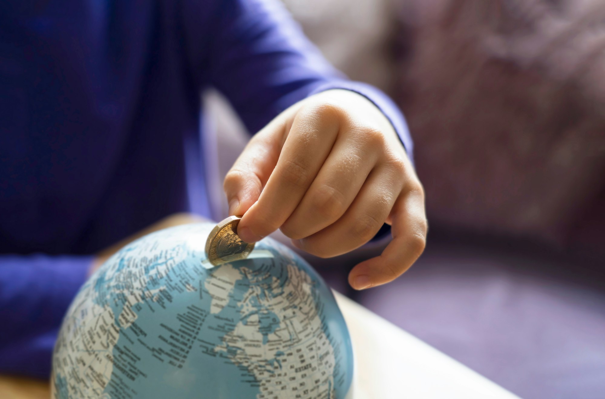 Les dons aux associations : quelles réductions d'impôts possibles ? Kid hand putting one pound coin into piggy bank to donate money helping the earth,Hand holding money